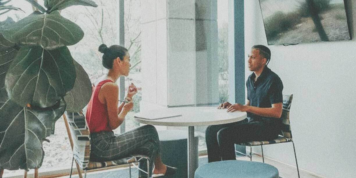 Woman in orange sitting and talking with a man in blue at a round table