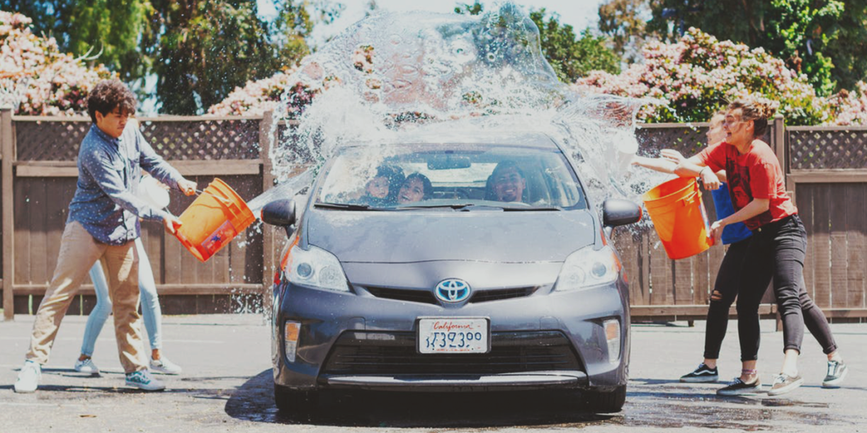 kids throwing buckets of water on a car